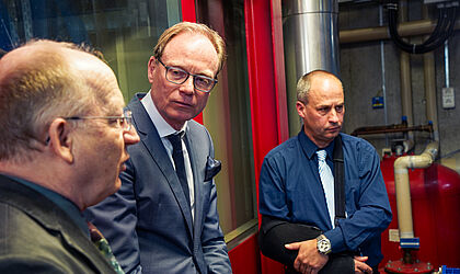Drei Männer, in der Mitte der Staatssekretär stehen in einer Werkstatt im Gespräch.