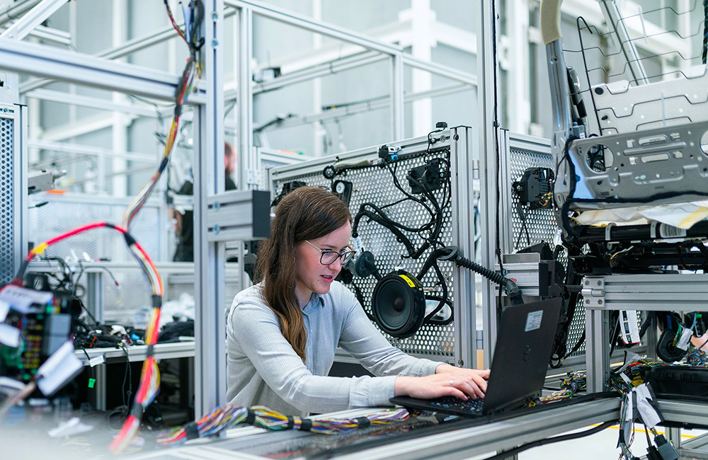 Studentin sitzt Elektroniklabor am Laptop umringt von Kabeln, Lautsprecher etc.