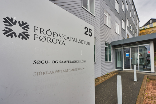 Nahaufnahme eines Gbäudeschilds der University of the Faroe Islands mit gläsernem Eingangsbereich