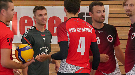 5 männliche Studierende der HOST-Volleyballer in roten Trikots im Gespräch