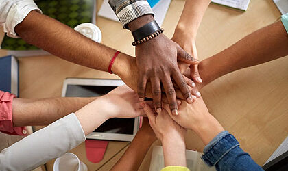 several hands of different skin colors placed on top of each other - as known from team sports