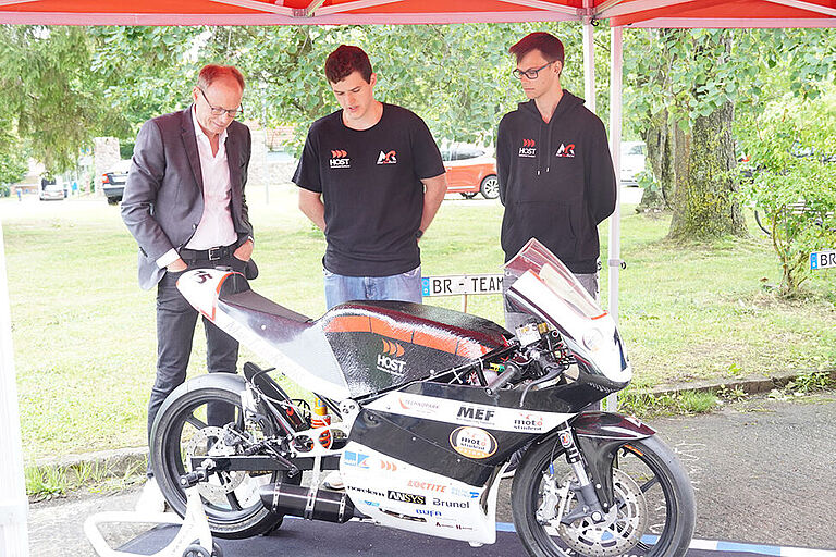 Staatssekretär Jochen Schulte im Gespräch mit 2 Studierenden des MariTeam-Rennteams mit ihrem E-Motorrad