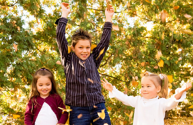 2 Mädchen und 1 Junge, die laubblätter nach oben werfen und lachen