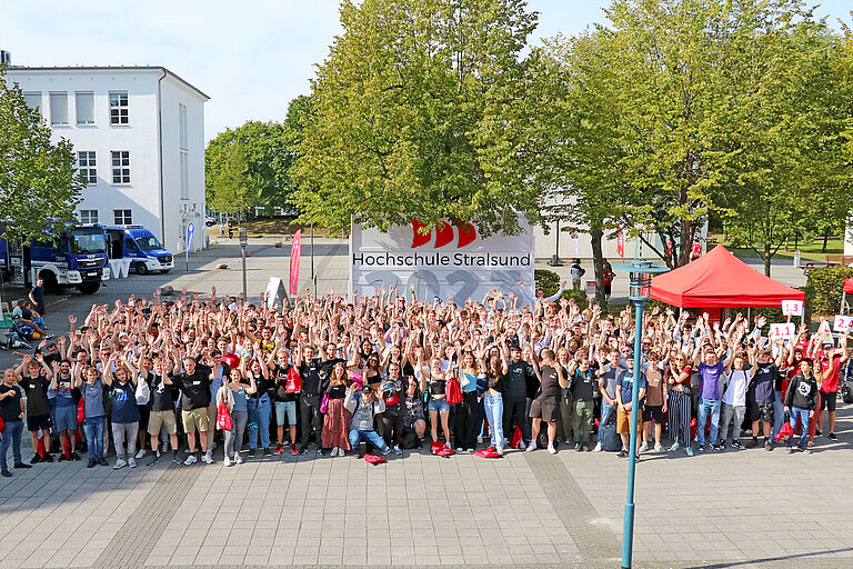 Ein Gruppenbild vieler junger Menschen von oben vor einem HOST-Schild.