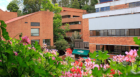 rote Backsteingebäude mir rotblütigen Blumen im Vorder- und Bäumen im Hintergrund