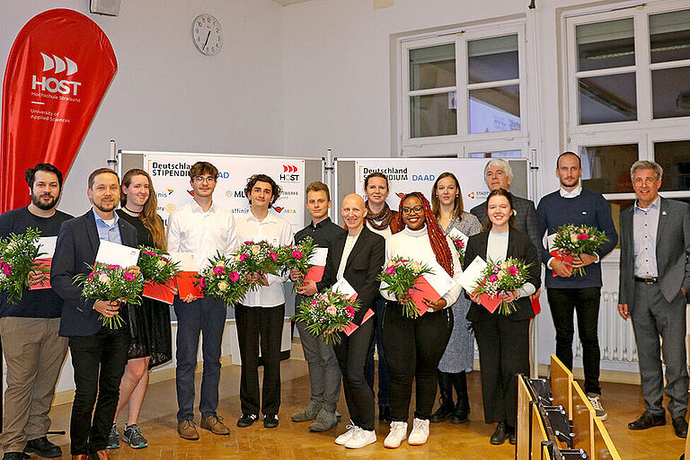 Ein Gruppenfoto von Stipendiat*innen mit Blumen und Fördermittelgeber*innen zur Verleihung des Deutschlandstipendiums 2023 an der HOST