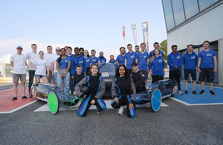 ca. 2 Dutzend Menschen vom ThaiGer-H2-Racing-Team in blauen Hoodies und dem Schüler-Team Greendrive mit 3 Rennwagen des Shell-Eco-Marathon