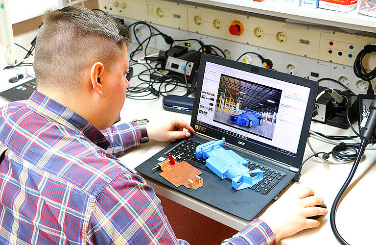 Mann im E-Technik-Labor, welcher am Laptop ein CAD-Model bearbeitet