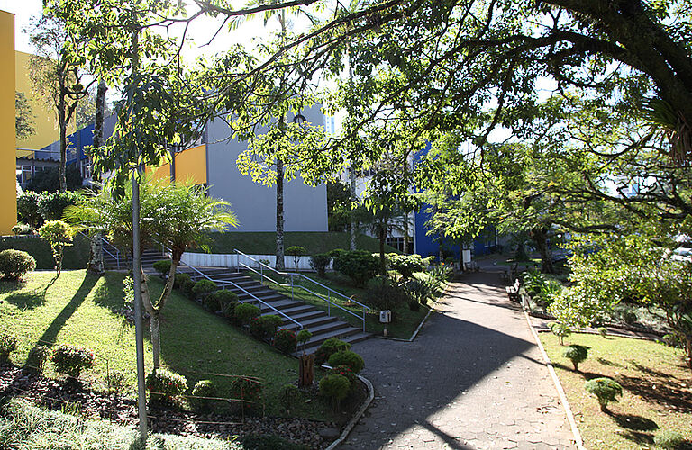 Campusgebäude der Universität Blumenau bei Tageslicht mit Bäumen und Bänken