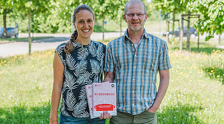 2 Personen im Grünen, die ein Buch in die Kamera halten