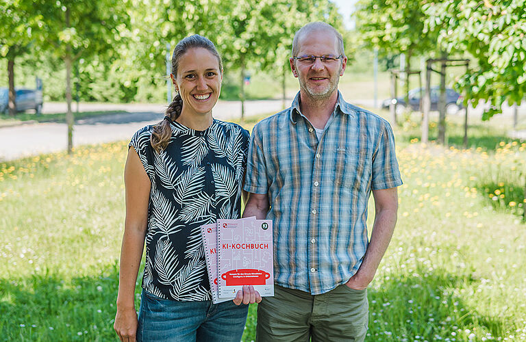 2 Personen im Grünen, die ein Buch in die Kamera halten