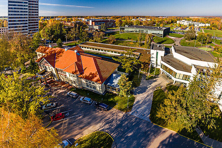 Luftaufnahme vom bewaldeten, grünen Hochschulcampus der Estonian University, mit mehreren Gebäuden und Parkplätzen