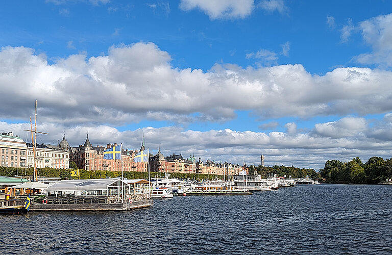 Städtkulisse und Hafen mit großen Booten und Anliegern bei bewölktem Himmel vom Wasser aus fotografiert