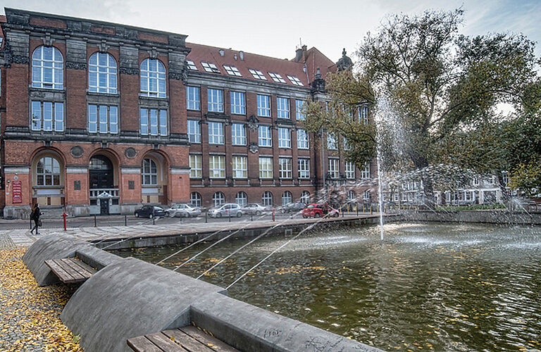 Ein rotes Backsteingebäude mit einem großen Spring-Brunnen davor.