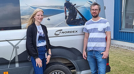 Christine Meyer und Jens Reppe vor einem Lieferwagen mit Fotoaufdruck einer Windkraftanlage