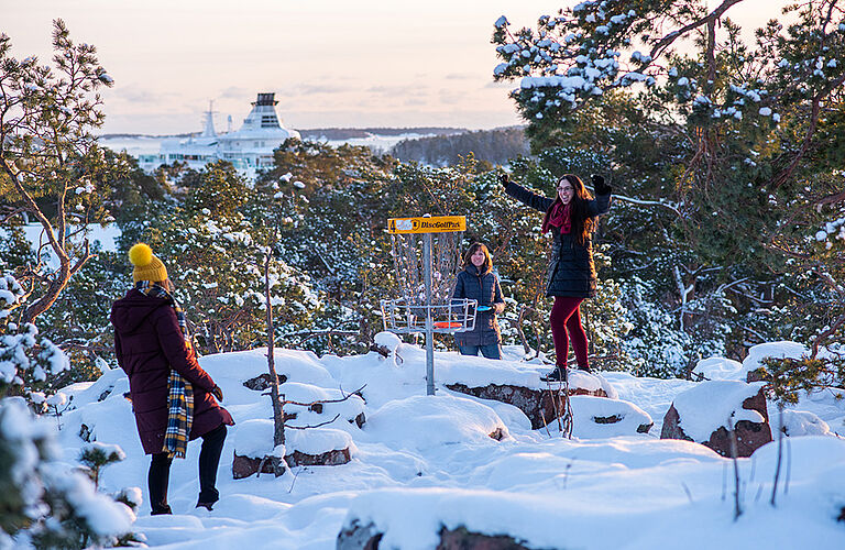 drei weibliche Studierende spielen Frisbee im Schnee und werfen in ein Frisbee-Tor