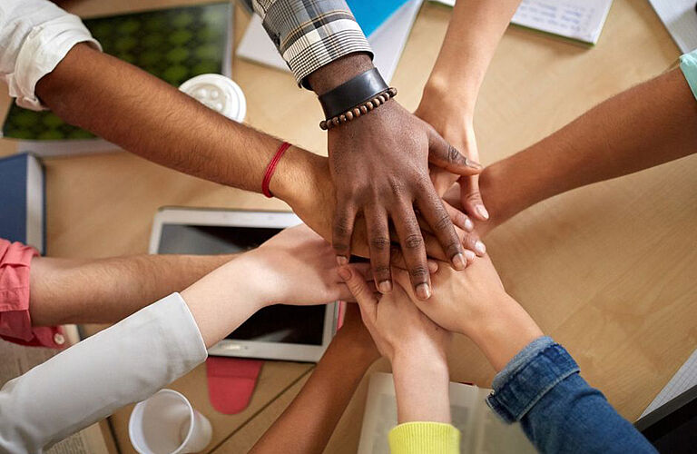 several hands of different skin colors placed on top of each other - as known from team sports