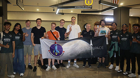 Eine Gruppe vorwiegend junger Menschen hält ein Banner mit einem Raketen-Logos des Sundspace in die Kamera.