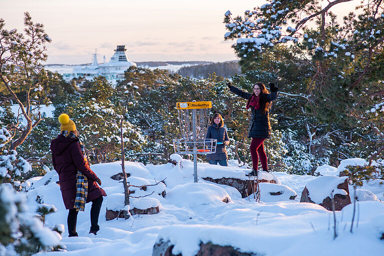 drei junge Frauen sind freudig in einer Schneelandschaft auf einer Erhöhung zu sehen.