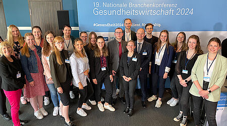 Gruppenfoto von 2 Dutzend Studierenden in Anzügen und Blaisern und Lehrenden der Fakultät für Wirtschaft vor einem Tagungsbanner