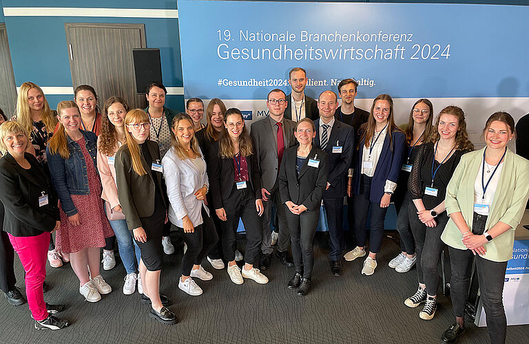 Gruppenfoto von 2 Dutzend Studierenden in Anzügen und Blaisern und Lehrenden der Fakultät für Wirtschaft vor einem Tagungsbanner