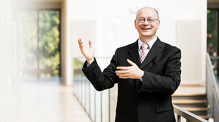 Prof. Michael Klotz im schwarzen Anzug auf einem Flur vor einem Treppengeländer