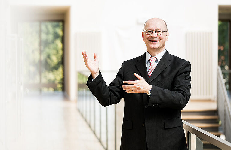 Prof. Michael Klotz im schwarzen Anzug auf einem Flur vor einem Treppengeländer