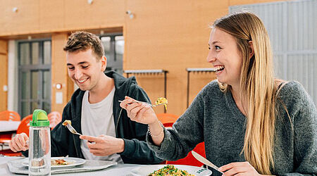 Nahaufnahme zweier lachenden Studierender, die in der HOST-Mensa sitzen und essen.