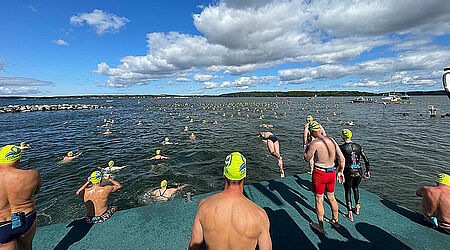 Blick auf den Strelasund mit unzähligen Schwimmern mit gelben Badekappen im Wasser und beim reinspringenzum Sundschwimmen 2021