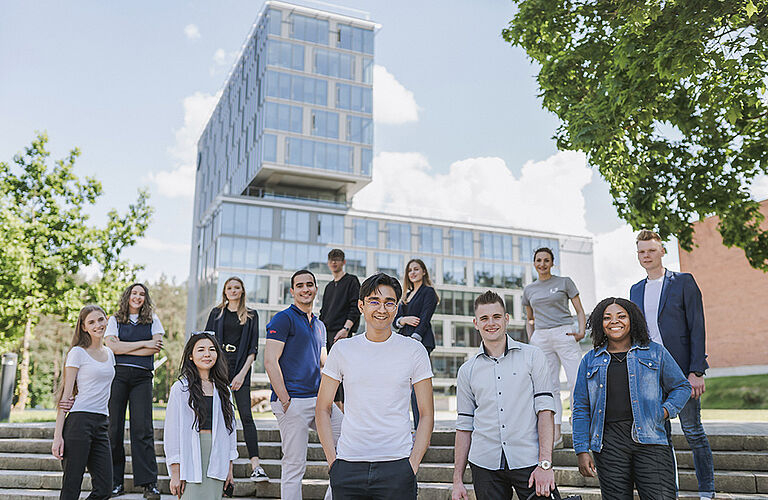 1 Dutzend Studierende auf einer Treppe vor einem Gebäude mit Glasfassade