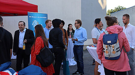 mehrere Menschen-Grüppchen im Gespräch und vor einem roten Pavillon auf dem Campus der HOST