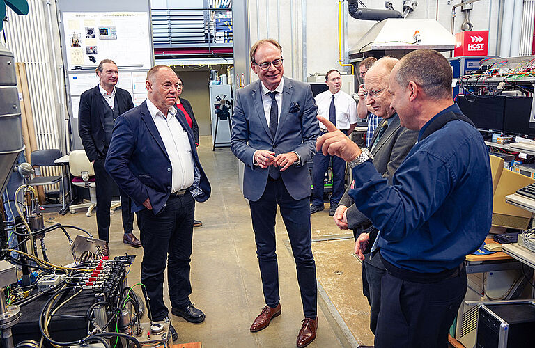 Gesprächsszene mit mehreren Männern in Anzügen in einer Werkstatt.