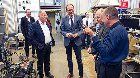 Gesprächsszene mit mehreren Männern in Anzügen in einer Werkstatt.