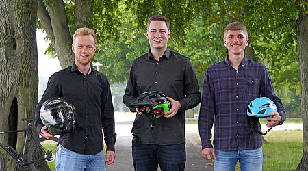 3 Gründer der Firma ACCIST mit Fahrradhelmen in der Hand in einer Alleestraße