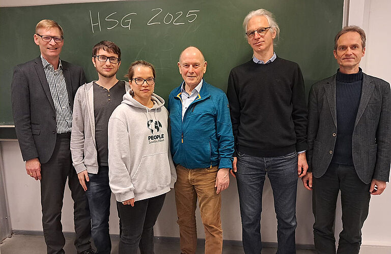 Sechs Menschen stehen vor einer grünen Tafel, an der "HSG 2025" angekreidet wurde.