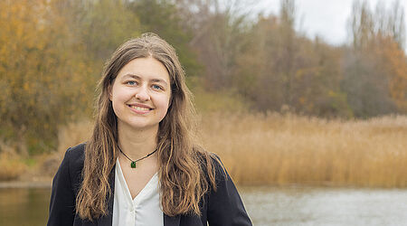 Portraitaufnahme von Julia Koch an einem See mit Bäumen im Hintergrund