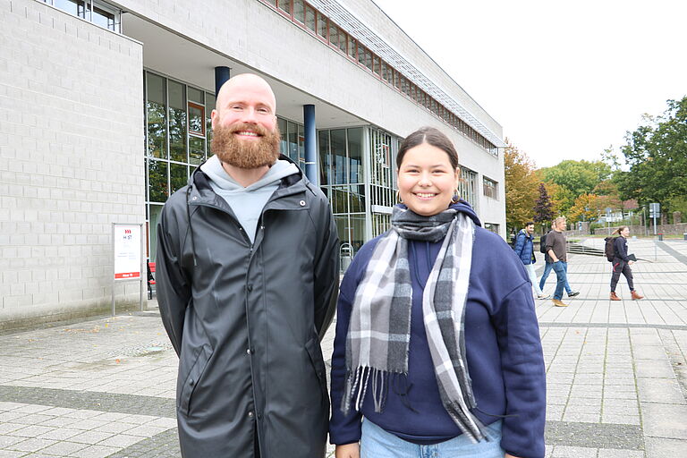 Ein Mann und eine Teenagerin stehen lächelnd vor der Hochschule