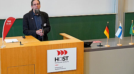 Prof. Johannes Gulden, in schwarzen Anzug, steht an einem Pult mit dem Logo Hochschule Stralsund, vor einer grünen Tafel.