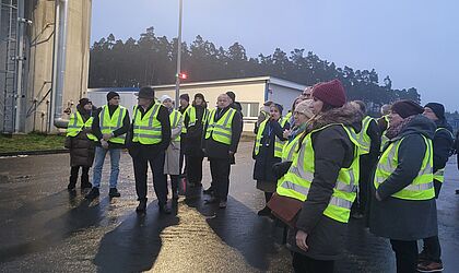 Mehrere Menschen mit Warnwesten bei regnerischem Wetter auf einer Außenanlage.