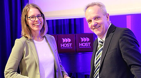 Anne Brorhilker und Prof. Thomas Eisgruber vor einem lilafarbenen Hintergrund beim Studium Generale der HOST