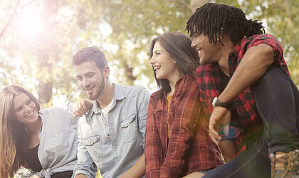 Vier lächelnde junge Menschen sitzen nebeneinander im Grünen - zwei Männer, zwei Frauen, international